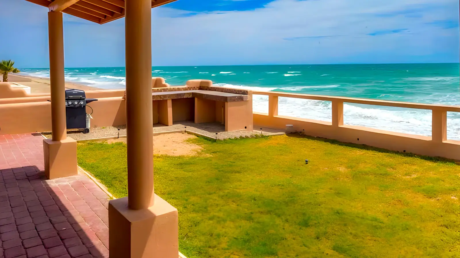 View from the porch of a Rocky Point home rental, overlooking a green lawn and the beach, with a bright blue sky in the background