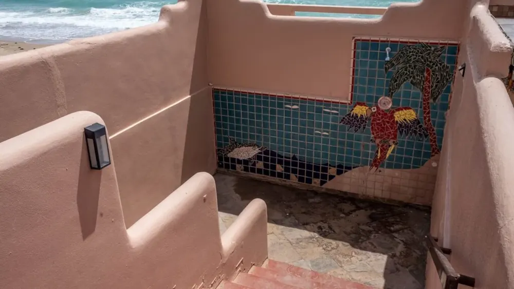 Salmon colored staircase descending to the beach with tile mural in the center.
